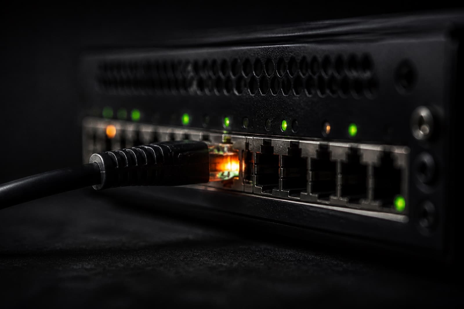 Close-up of a black network switch and a faintly glowing cable